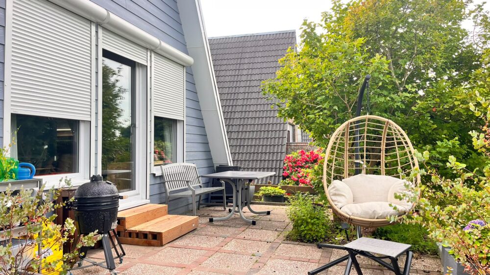 Terrasse mit Hängesessel und Grill am blauen Haus